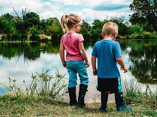zwei Kinder stehen in Gummistiefeln an einem See